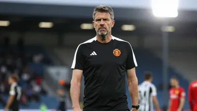 A tight waist-up shot of an anonymous 40-year-old male Newcastle United coach in a black and white kit, with a serious...