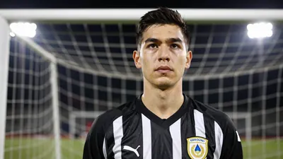 Photorealistic image of a 34-year-old goalkeeper in a black and white striped jersey, standing in a goalmouth with a...