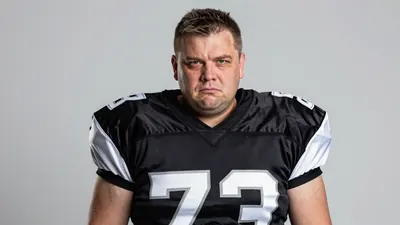 A 40-year-old man with a strong build and a determined expression, wearing a black and white football kit, in a well-lit...
