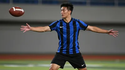 A 22-year-old male football player in a solid blue and black striped jersey, standing in a defensive stance with arms...