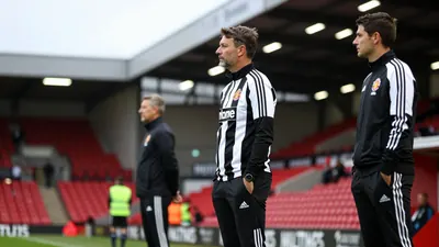 A 30-year-old, anonymous Newcastle United assistant coach, wearing a black and white striped tracksuit, stands on the...