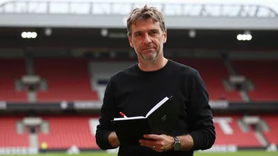 A photorealistic image of an anonymous, 40-year-old, German football manager, wearing a black, long-sleeved, cotton...