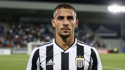 A photorealistic portrait of a 30-year-old male football defender, wearing a black and white striped jersey, standing on...