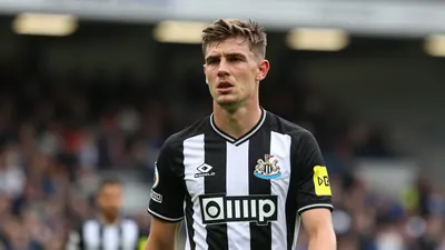 A young, focused Newcastle United striker in his mid-20s, clad in the iconic black and white striped home kit with the...
